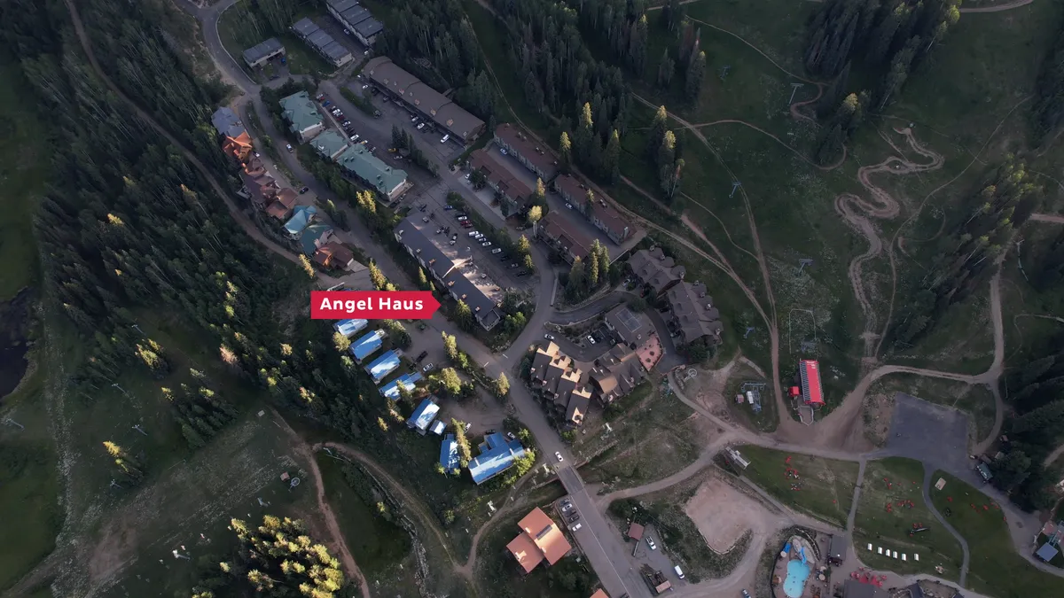 An exterior shot of Angel Haus and surrounding lodges, set amid a forested area with visible roadways. The scene feels adventurous and welcoming, suggesting easy access to outdoor activities and a community of vacationers ready to explore.