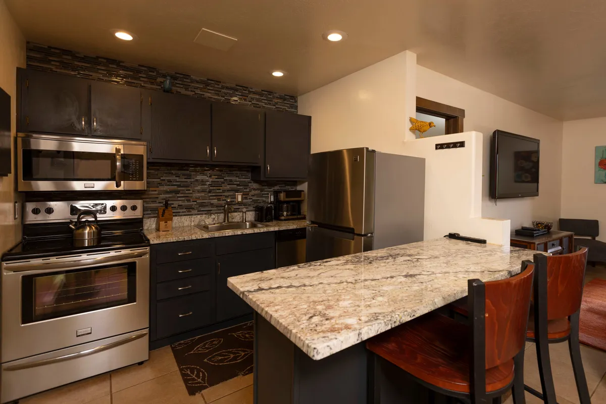 A cozy, modern kitchen with a generous granite countertop, stainless steel appliances, dark cabinetry, and a textured backsplash. The space is clearly designed for both cooking and socializing, with enough room to prepare meals and entertain family members.