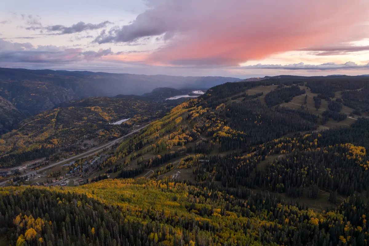A sweeping view of rolling hills adorned with vibrant autumn foliage, distant mountains, and a tranquil water body. The serene mood invites reflection and appreciation of the natural beauty surrounding the resort.