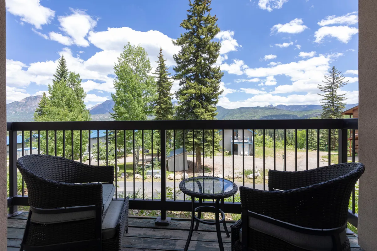 This image shows a serene exterior balcony with comfortable seating, overlooking lush greenery and a breathtaking mountain view. The scene evokes relaxation, with the mountains as a backdrop and plenty of natural light inviting guests to unwind and soak in the scenery.
